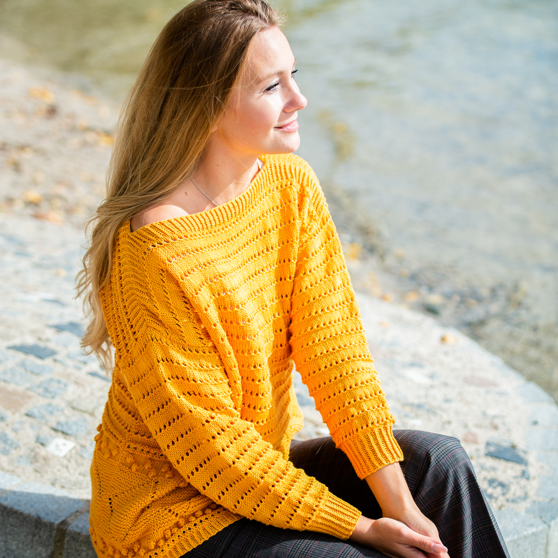 seitlich sitzende Frau mit gelbem Sommerpulli am See