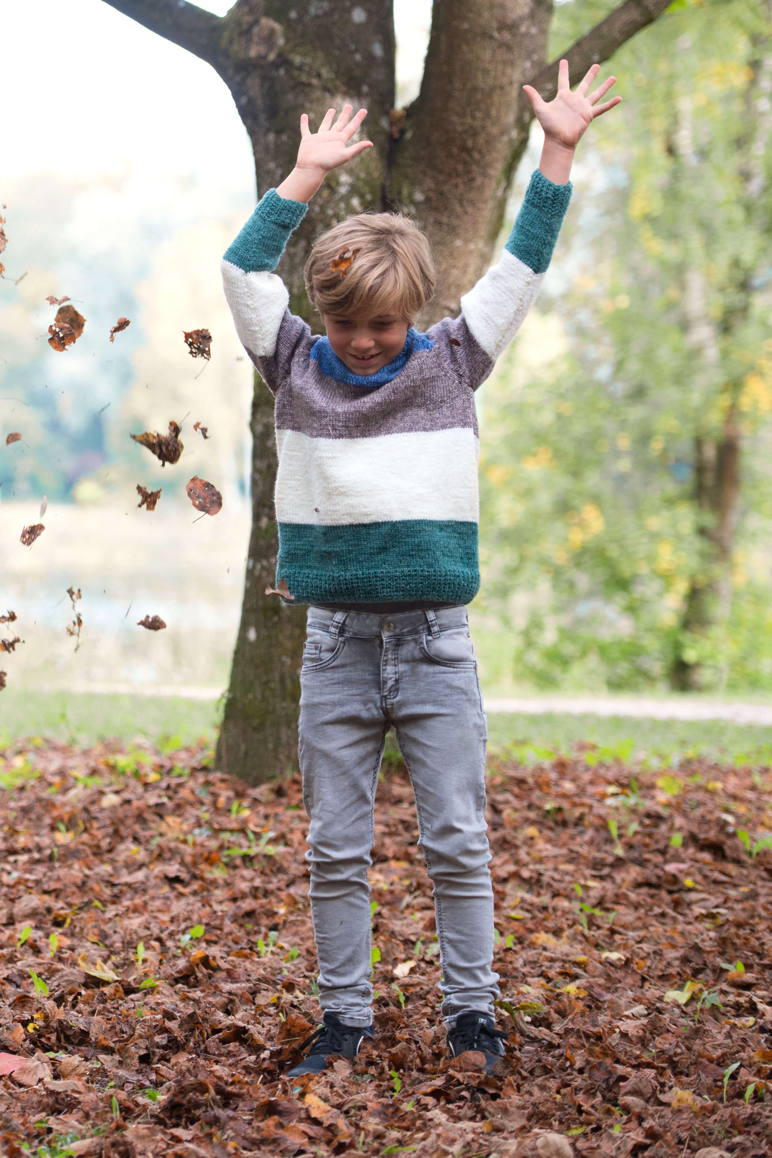 Junge im gestreiften und gestricktem Pulli beim Blätterhochwerfen im Herbst