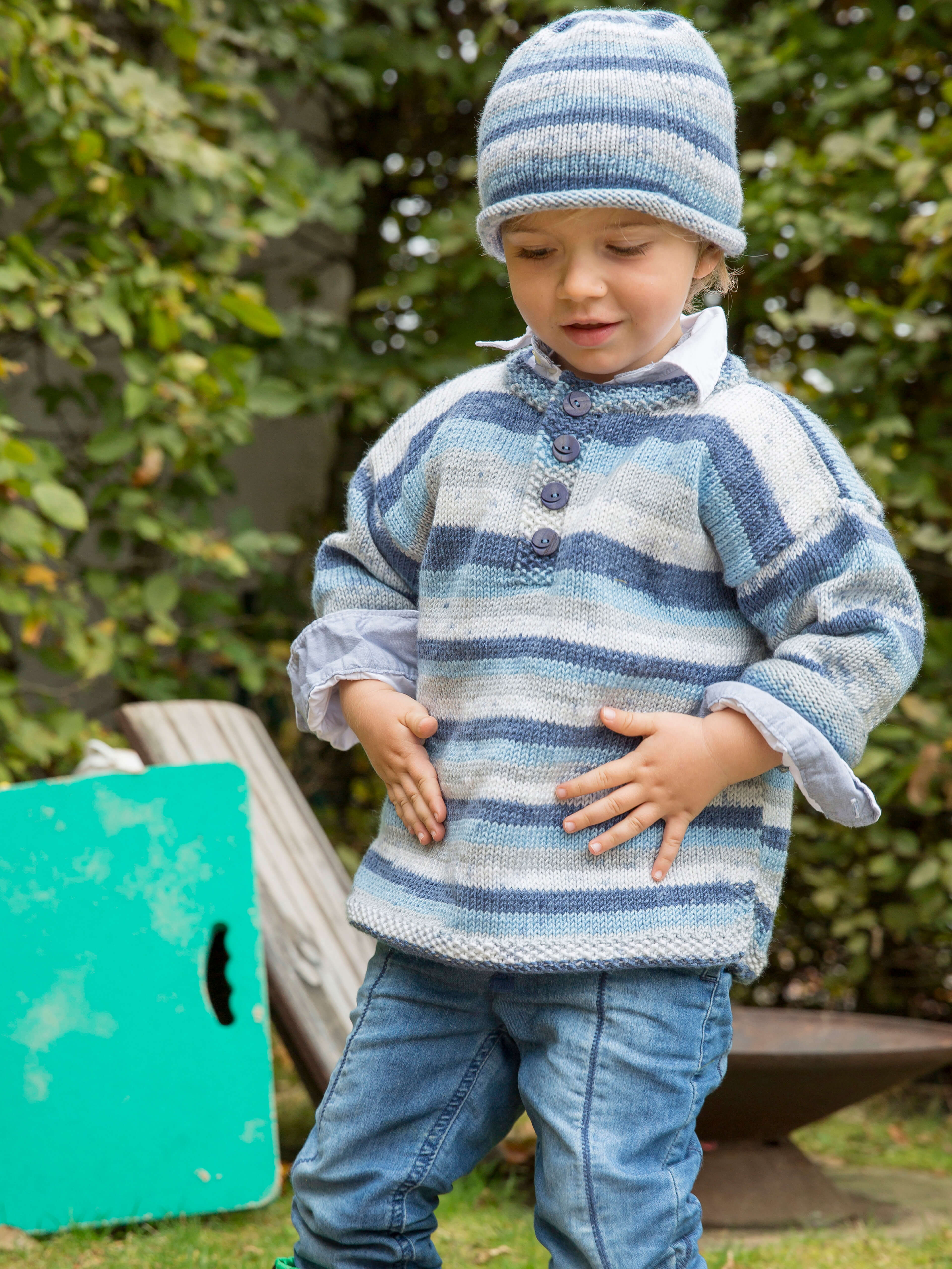 kleiner Junge spielend im Garten mit Pulli und passender Mütze