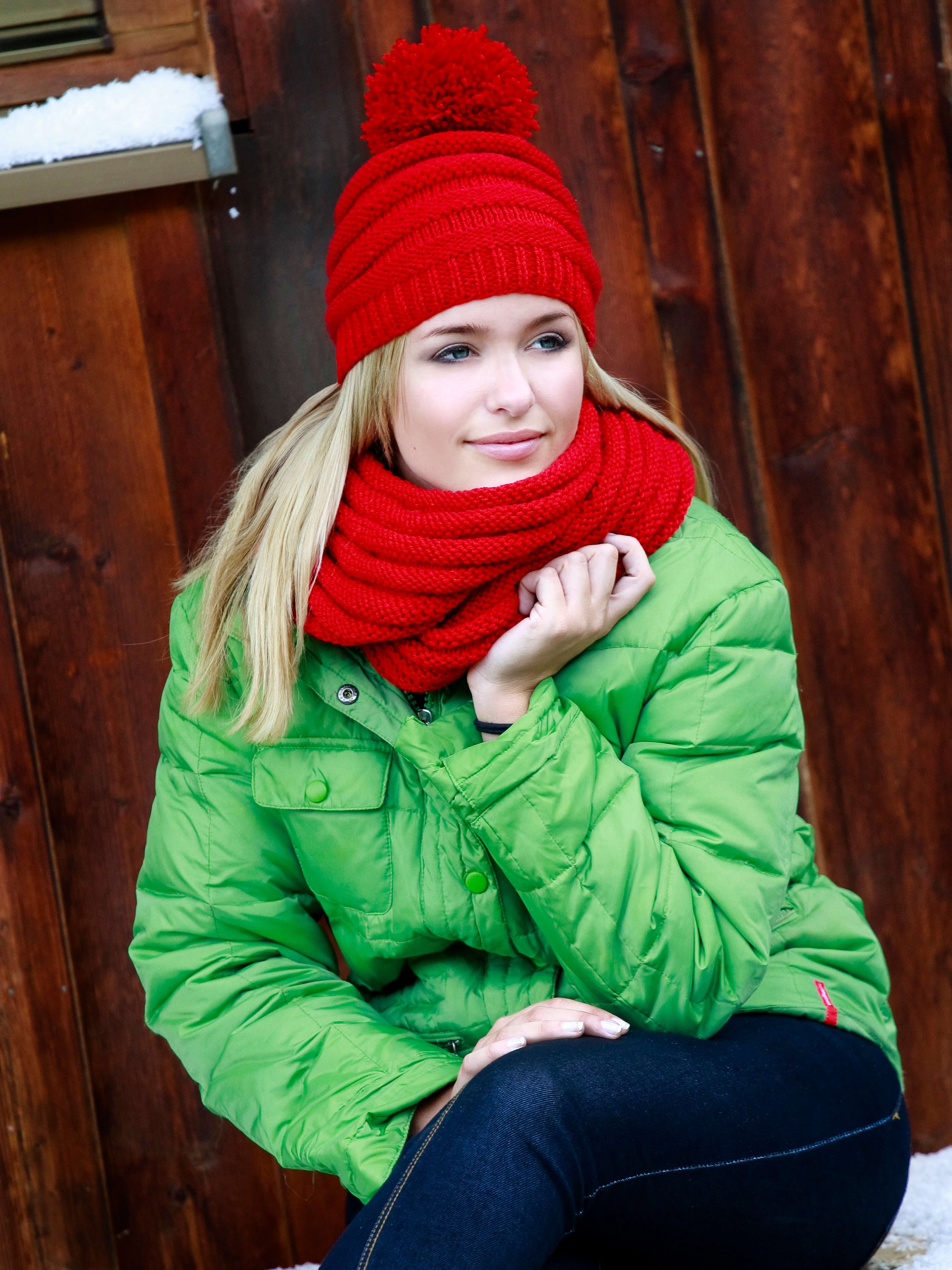 blonde Frau mit grüner Jacke und rotem Schal sowie Mütze