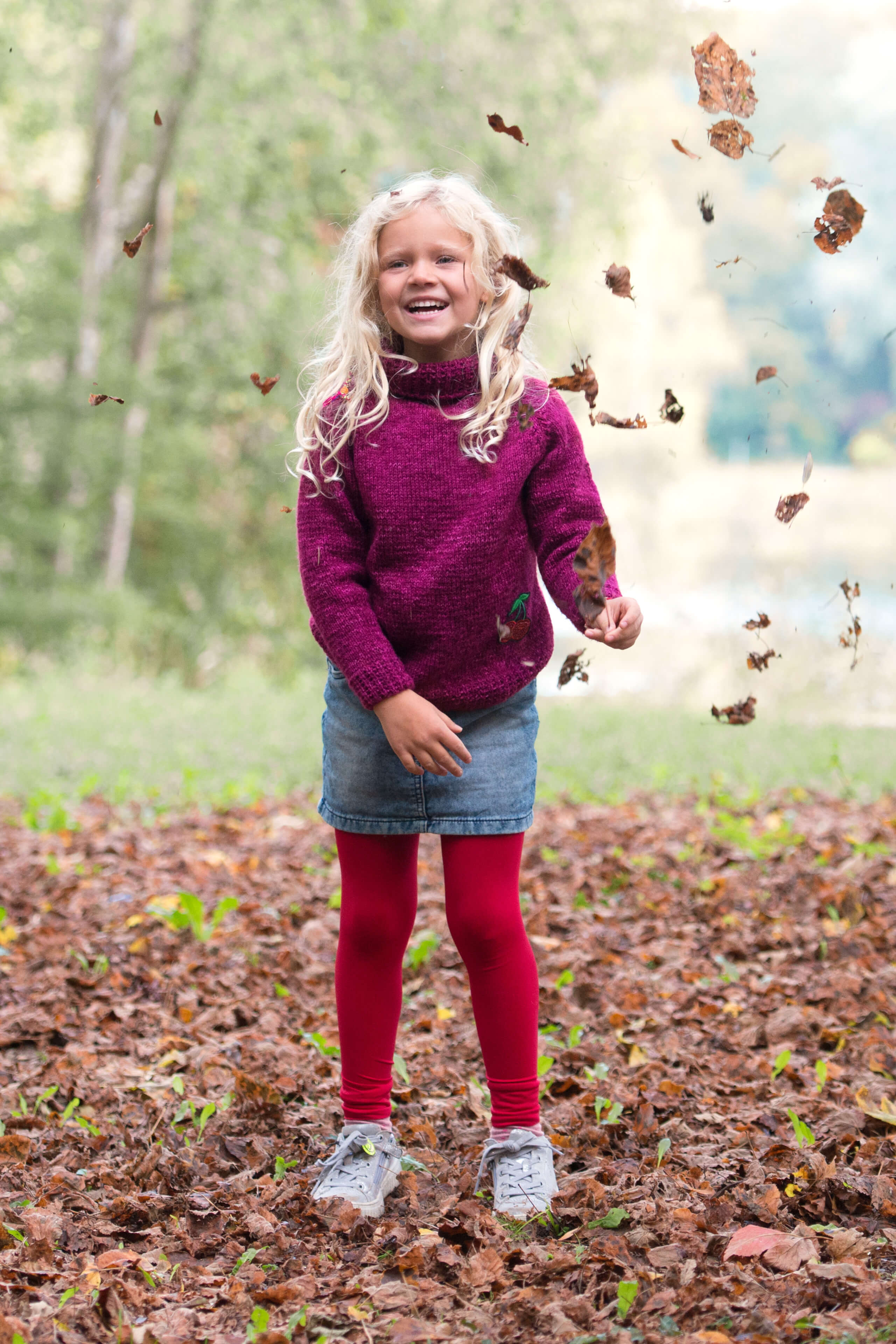 Mädchen im Pulli und roter Strumpfhose  beim Blätterspaß im Herbst