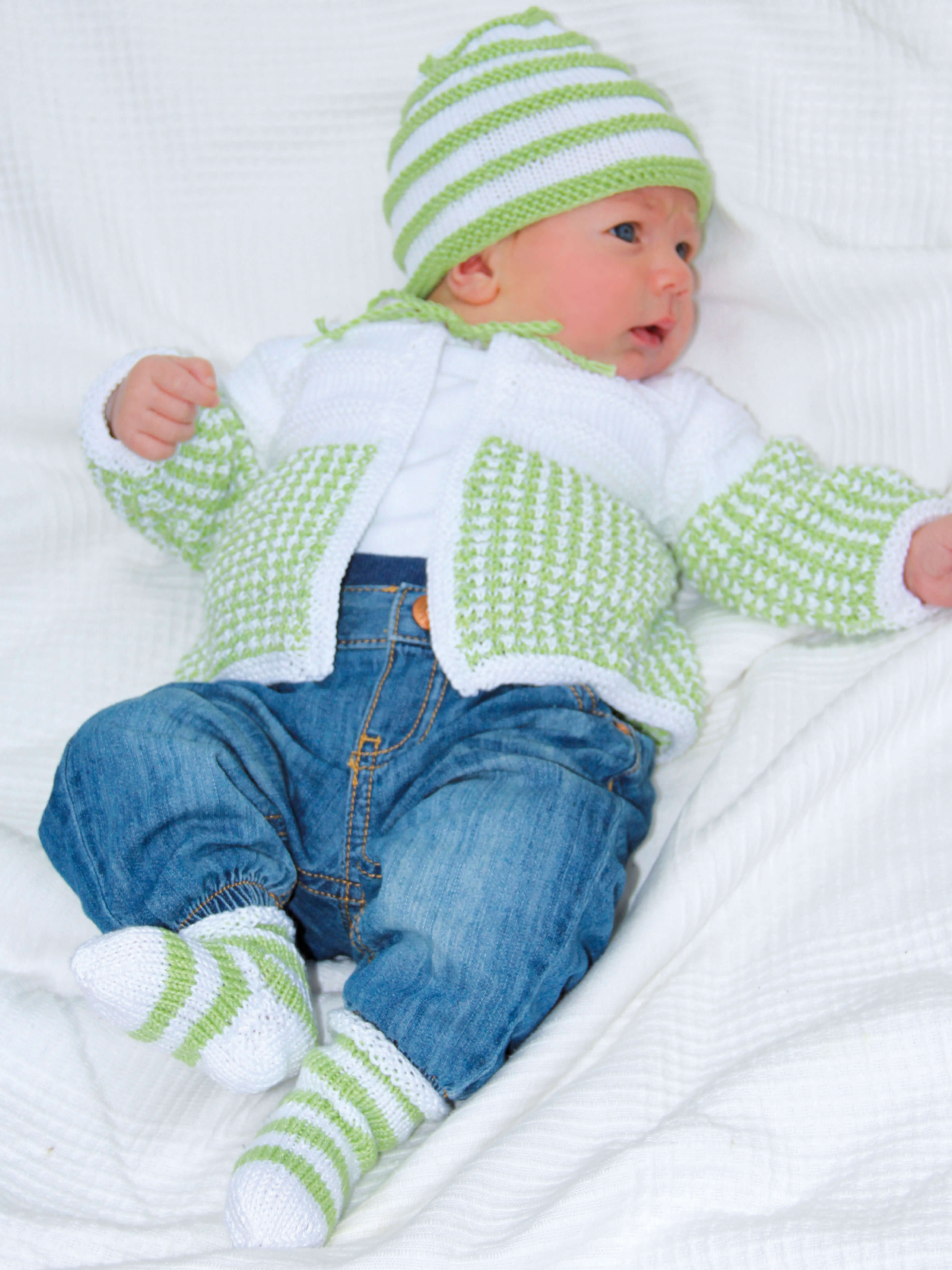 Baby in weiß-hellgrün gestricktem Jäckchen mit passender Mütze und Socken aus Cotton Quick uni Wolle von Gründl