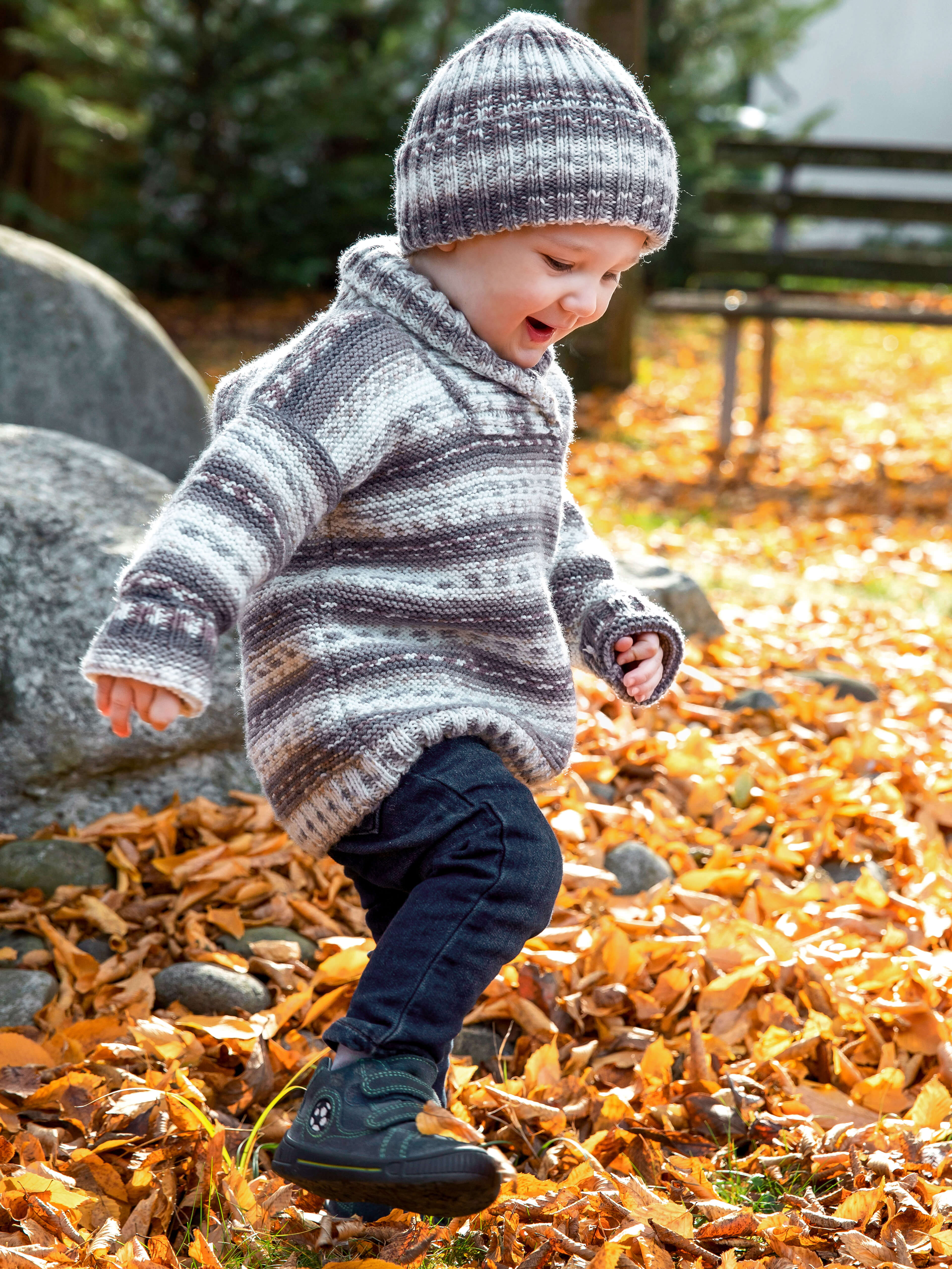 Kleinkind in gestricktem, dicken Pullover und passender Mütze im Herbstlaub aus der Gründl Wolle Baby color