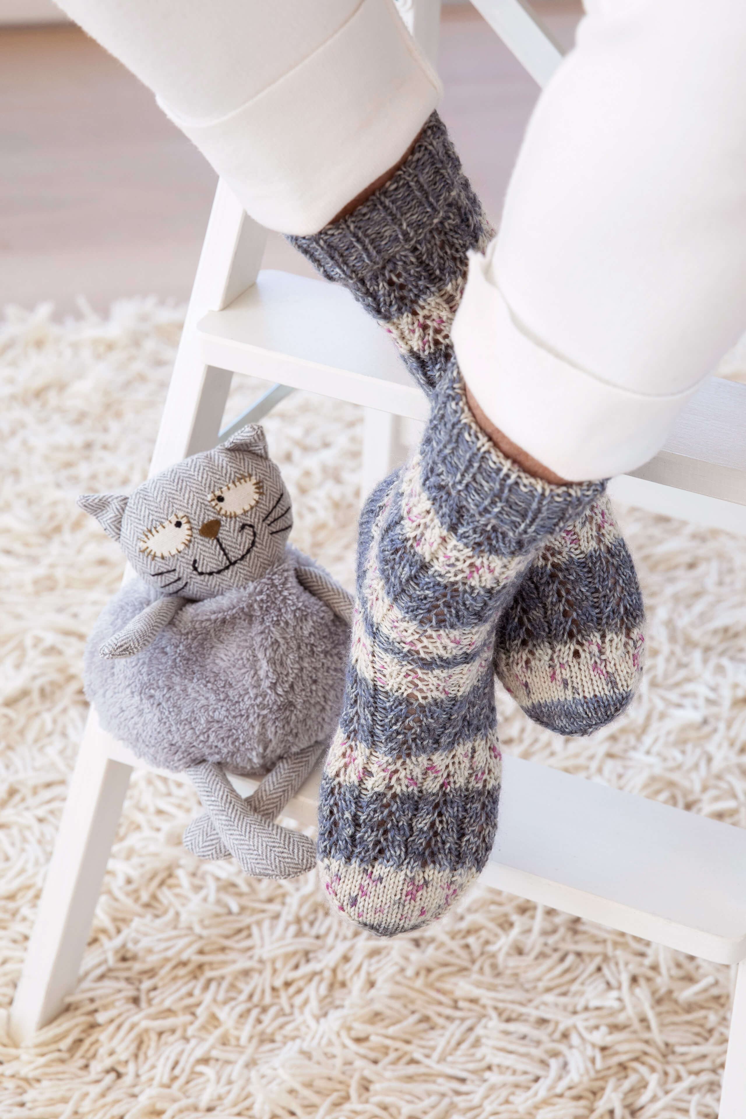 grau-weiß gestreifte Socken im Lochmuster  neben einer Kuscheltier Katze