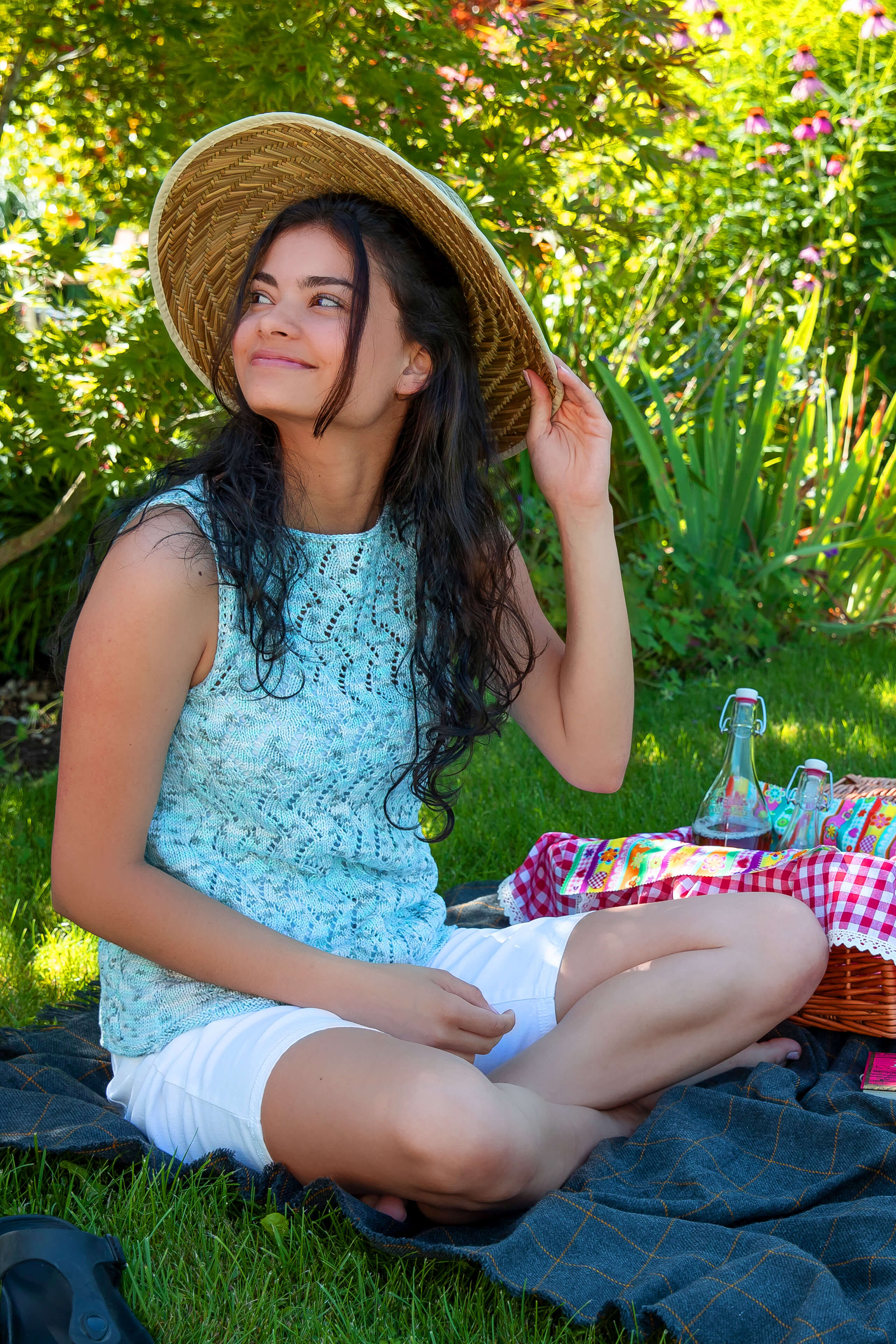Frau mit großem Sommerhut und türkis farbenden Sommertop beim Picknick