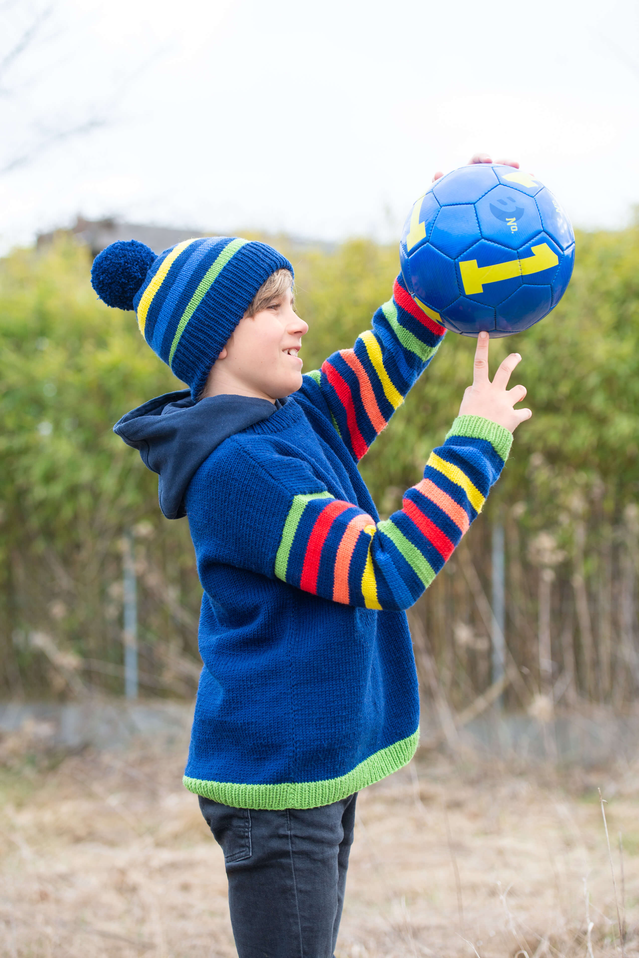 Junge am Ballspielen  mit selbstgemachtem Pulli und Mütze