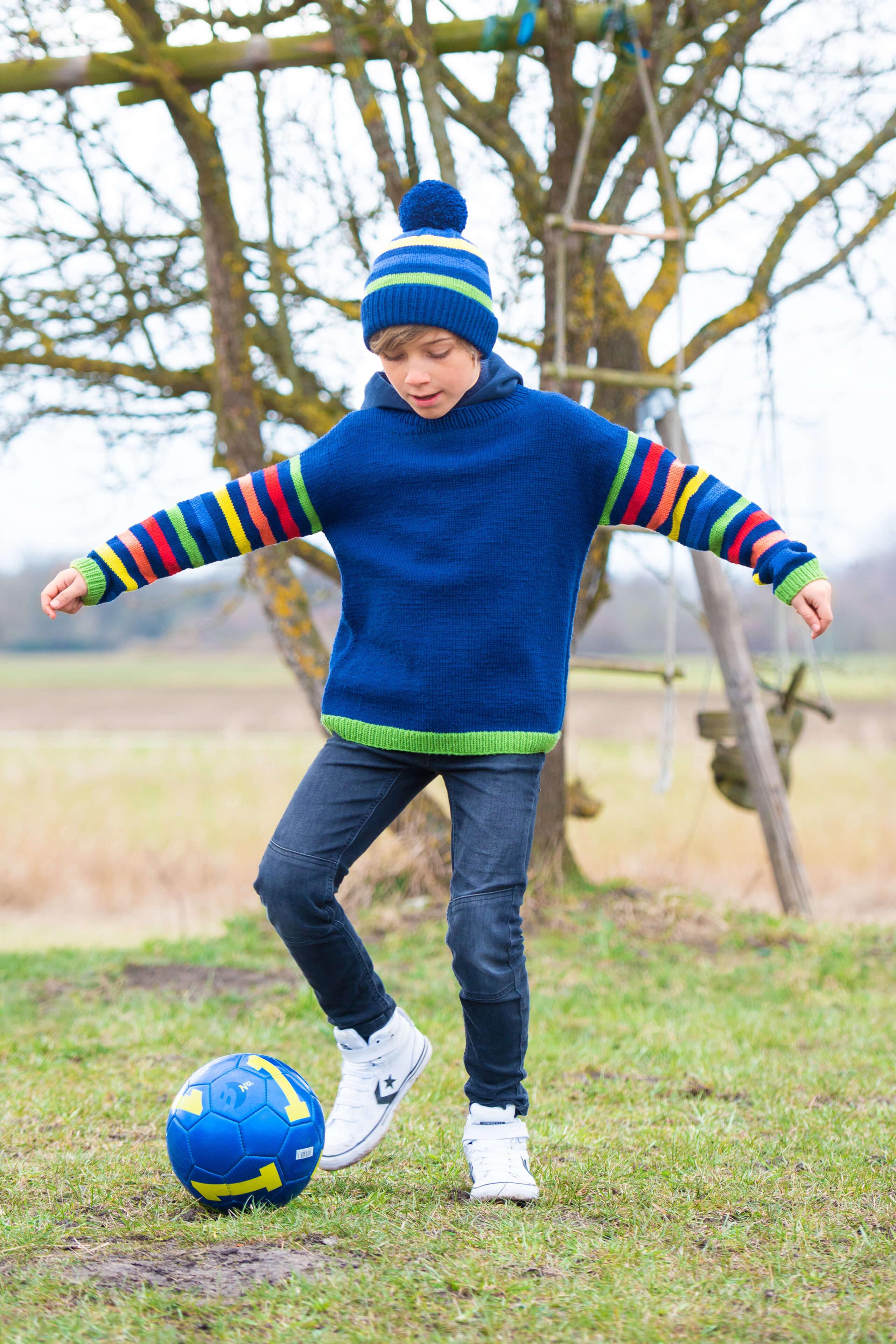 Junge mit Mütze und Pulli beim Fußballspielen