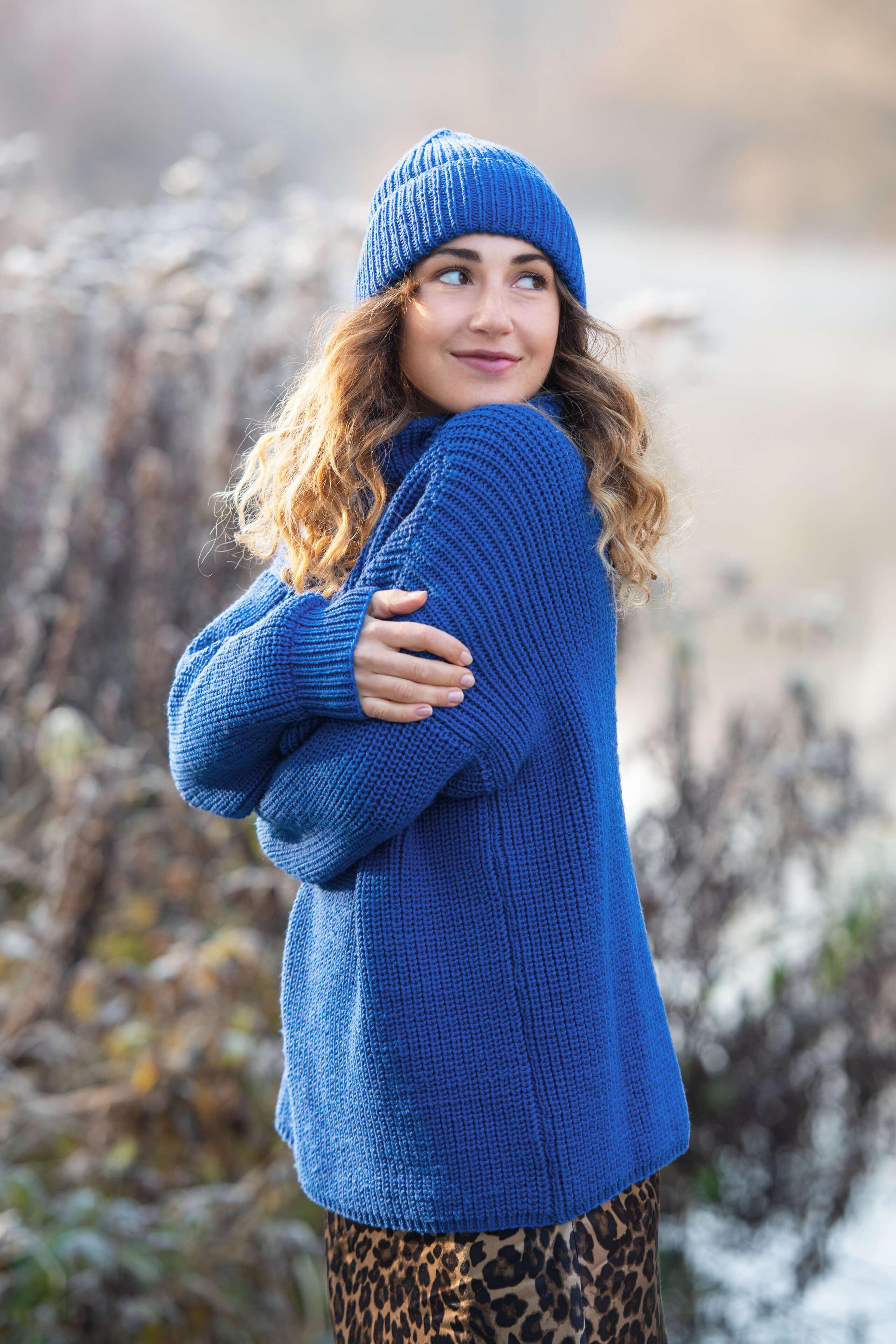 umschauende Frau mit royalblauem Pullover und passender Mütze in winterlciher Umgebung